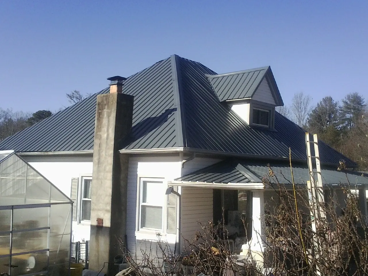 Dark blue standing seam metal roof on a white farmhouse with dormer — Slate & Tile Roof Repair by Roofing Brothers in Ranchos De Taos