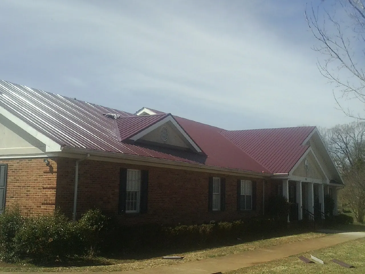 Red metal roof with gabled entries on a long brick building, from a Hail Damage Roof Repair job in Ranchos De Taos