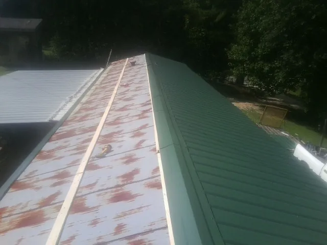 Old rusted panels beside newly installed green metal roofing — Wind Damage Roof Repair by Roofing Brothers in Ranchos De Taos