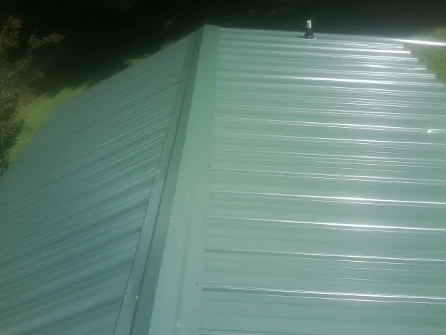 New green metal panels meeting at the ridge of a roof — Flat Roof Repair work by our crew in Ranchos De Taos