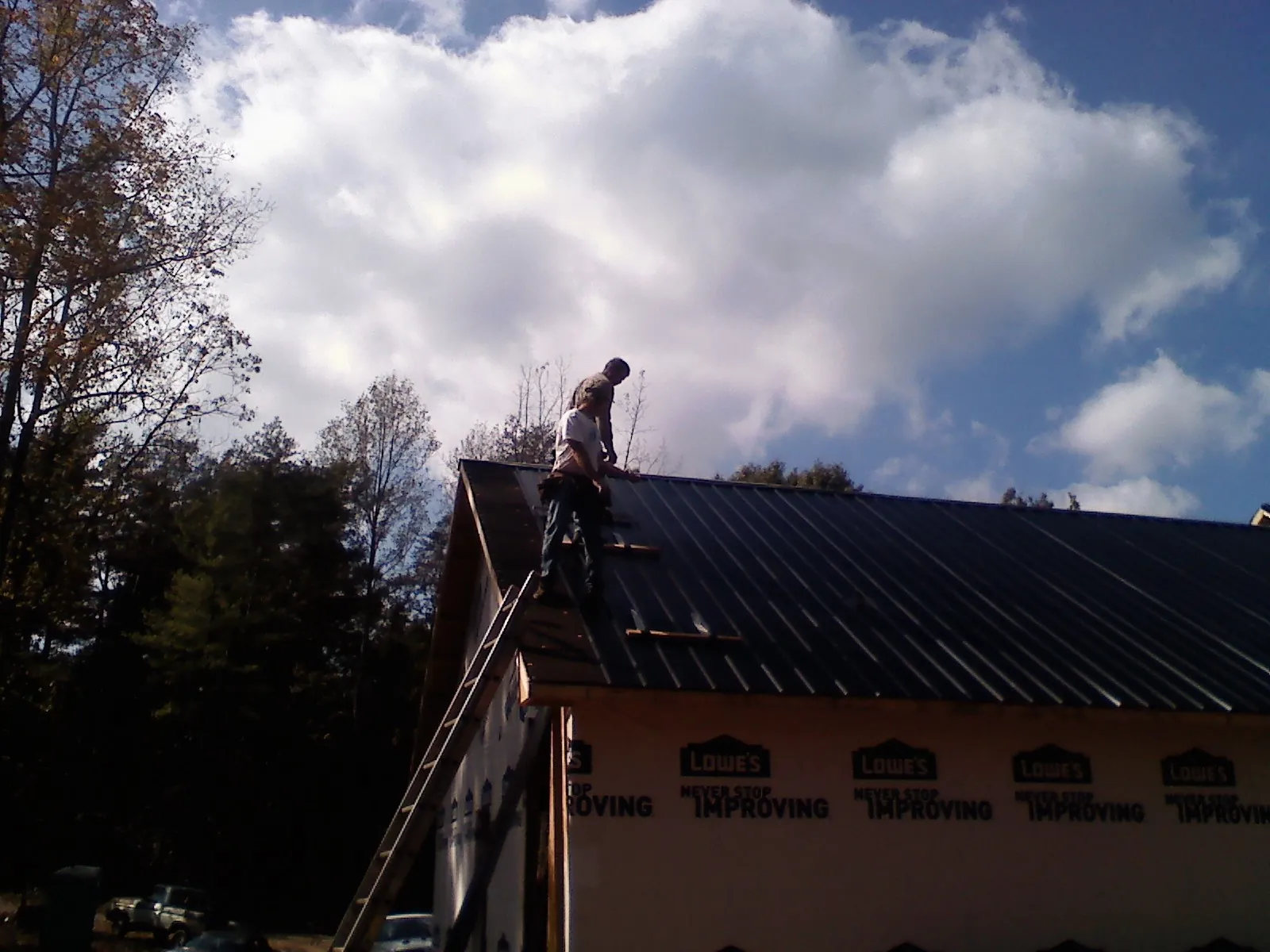 Roofer fastening dark metal panels high against a cloudy sky, from a Roof Inspection job in Ranchos De Taos