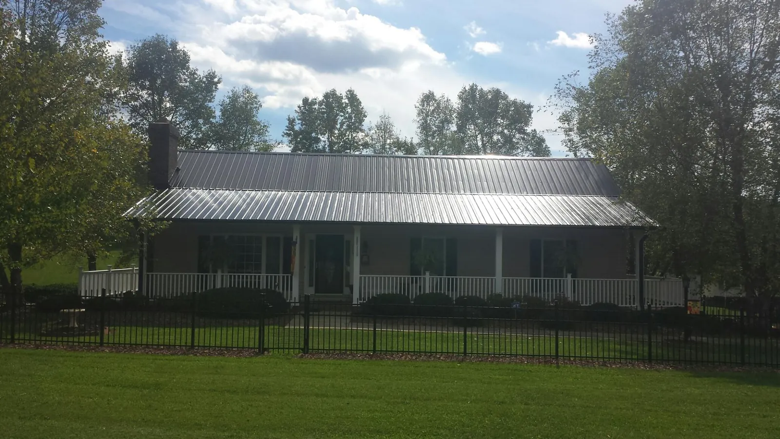 Gray metal roof on a brick ranch with a full width front porch — Gutter Guard Installation work by our crew in Ranchos De Taos