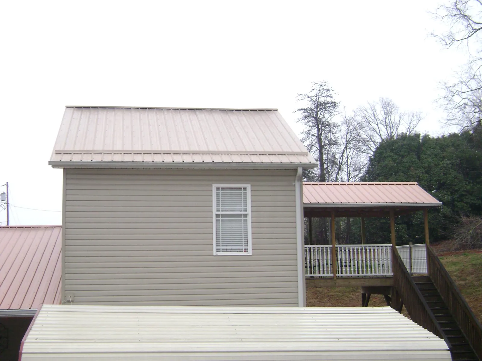 Tan metal roofs on a two story addition and attached porch, from a Roof Replacement job in Ranchos De Taos