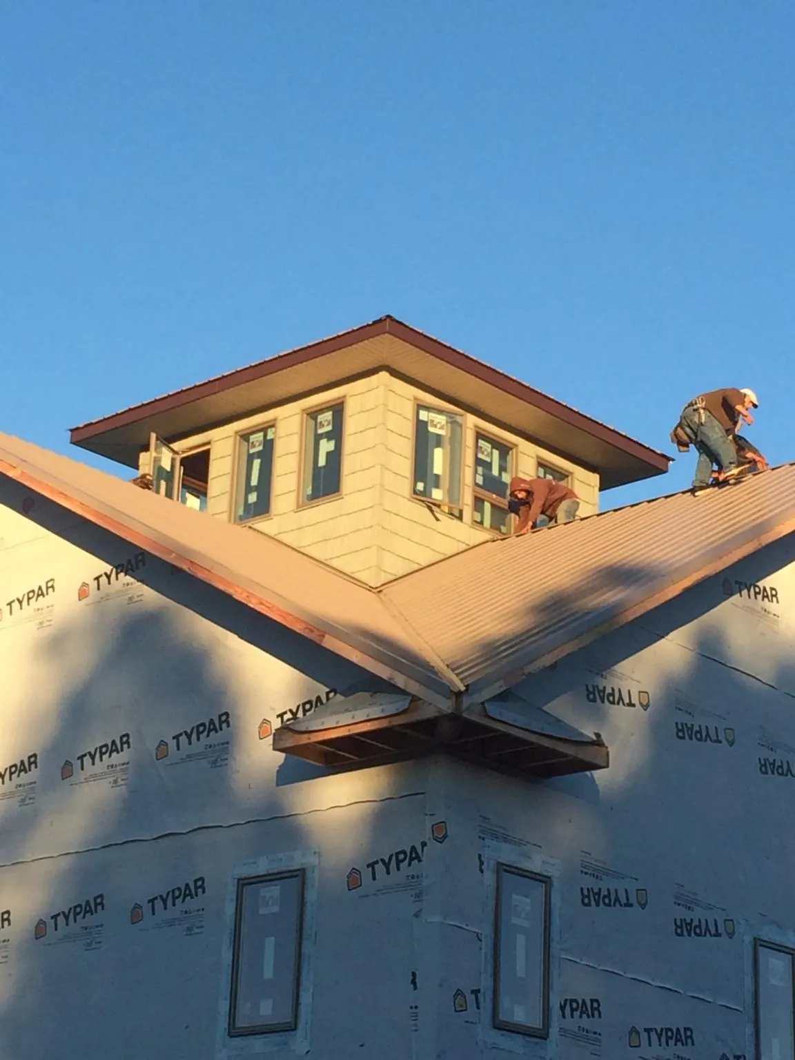 Roofers working around a rooftop cupola on a new metal roof at sunset — Roof Waterproofing in Ranchos De Taos by Roofing Brothers